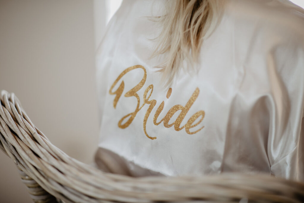 Bride wearing a silky white robe with gold lettering – intimate and stylish inspiration for wedding bridal shower ideas